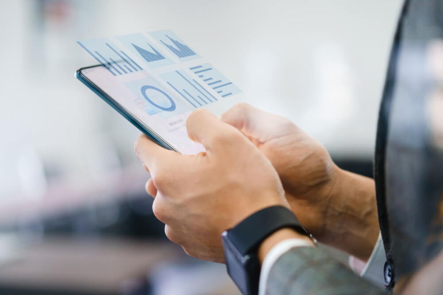 Two hands hold a cell phone on which various graphs and diagrams can be seen