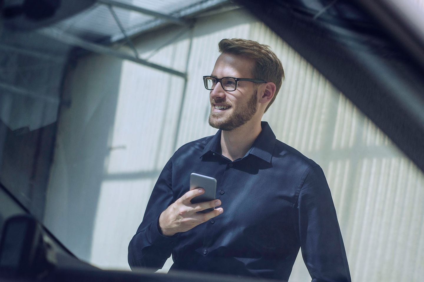 Uitzicht vanuit een auto op een glimlachende man met bril en mobiele telefoon in de hand