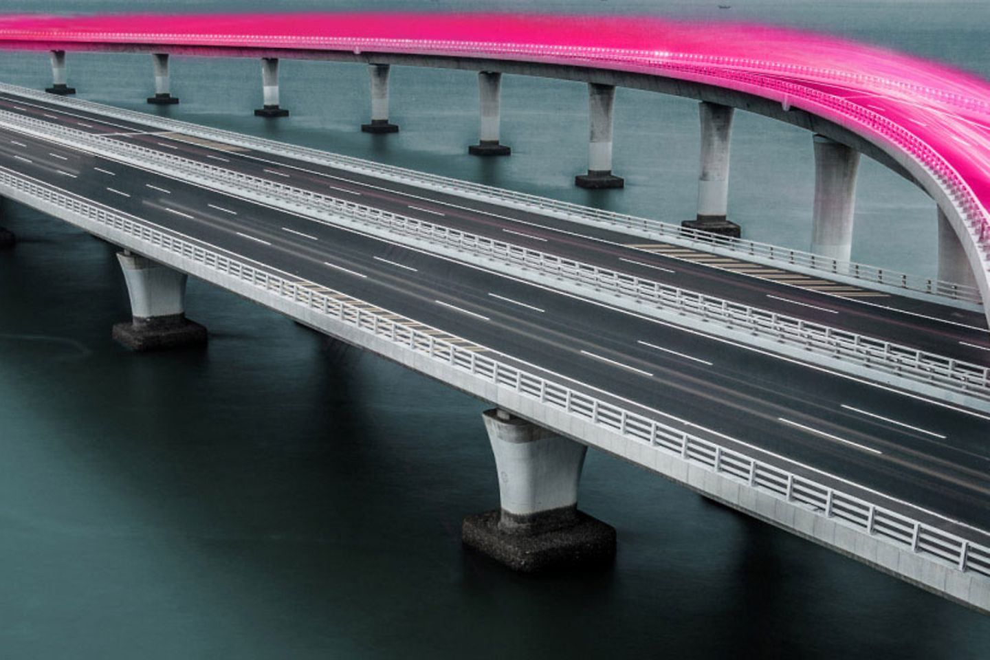 Brücke über das Meer mit verschwommenen magenta Rücklichtern von Autos 