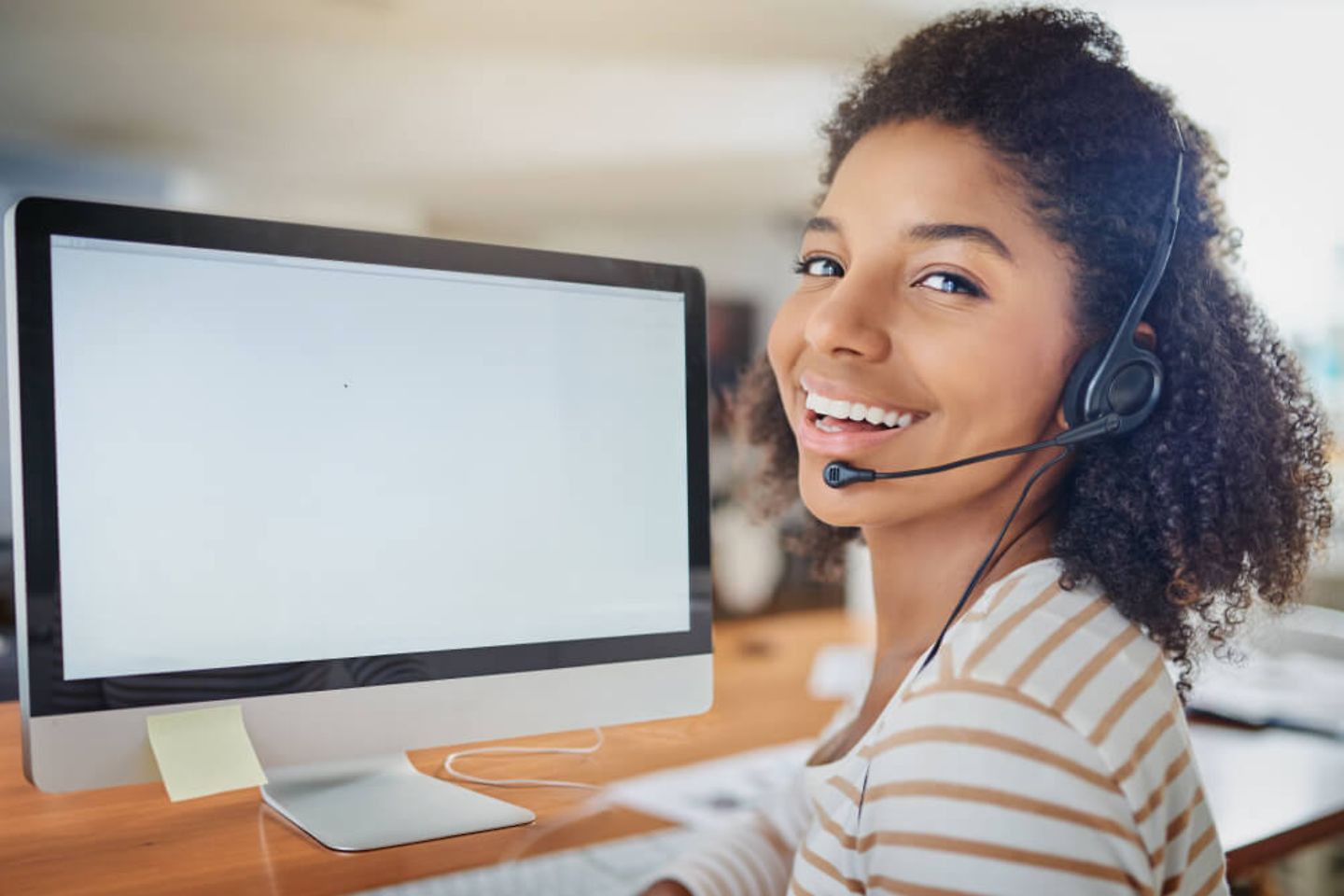 Eine Frau sitzt vor einem Monitor, trägt ein Headset und lächelt