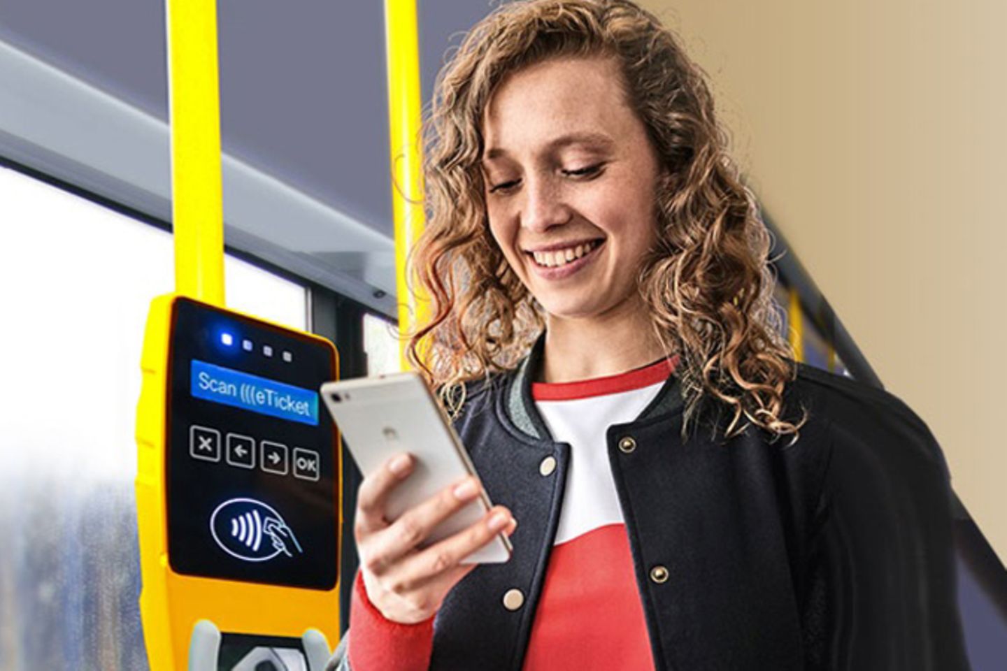 A woman is standing on a bus next to a contactless ticket machine, looking at her smartphone.