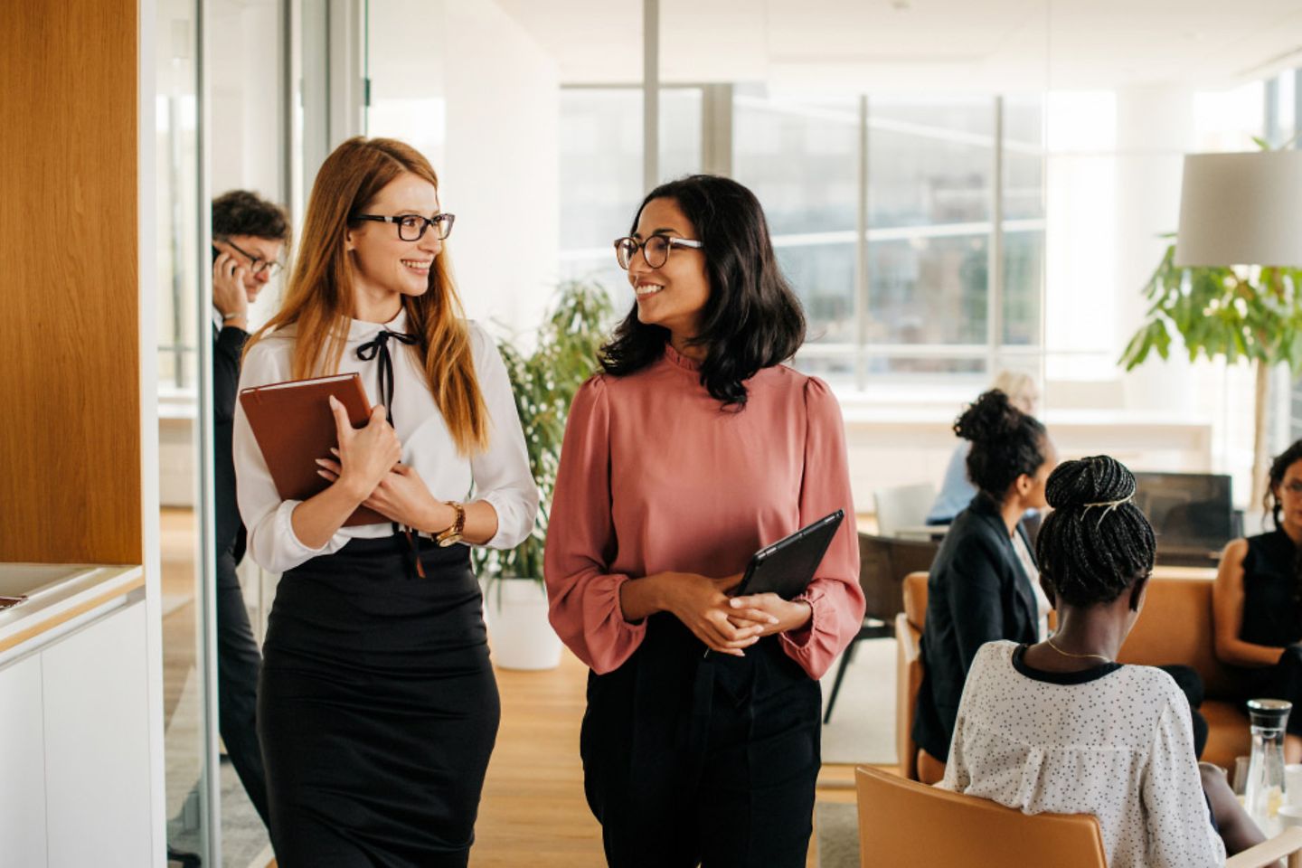 Two Women are walking next to each other in an office, both are smiling 