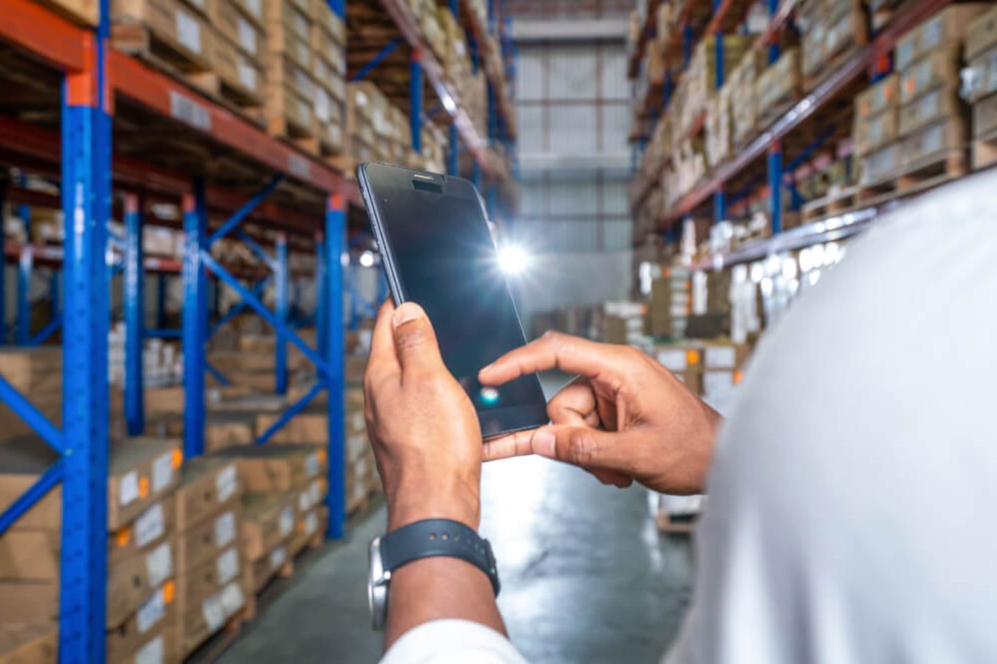 Man holding a smartphone, a warehouse can be seen in the background.