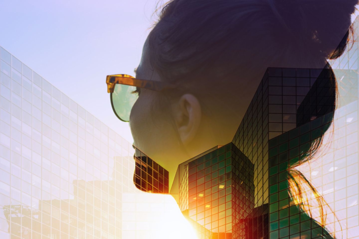 Femme avec des lunettes de soleil devant un soleil couchant, regardant des immeubles de bureau