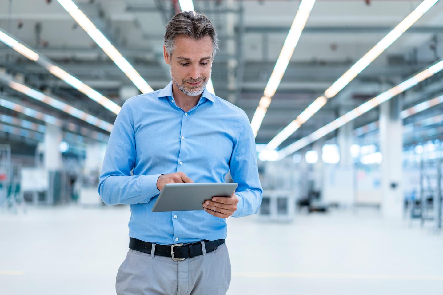 Man in blauw overhemd kijkt op zijn tablet in fabriek