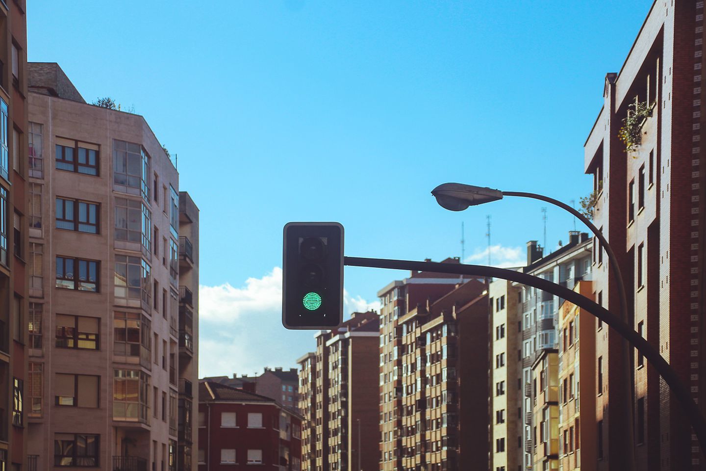 Straßenschlucht bei Tag in einer Großstadt ohne Verkehrsteilnehmer. In der Bildmitte ist eine grüne Ampel.