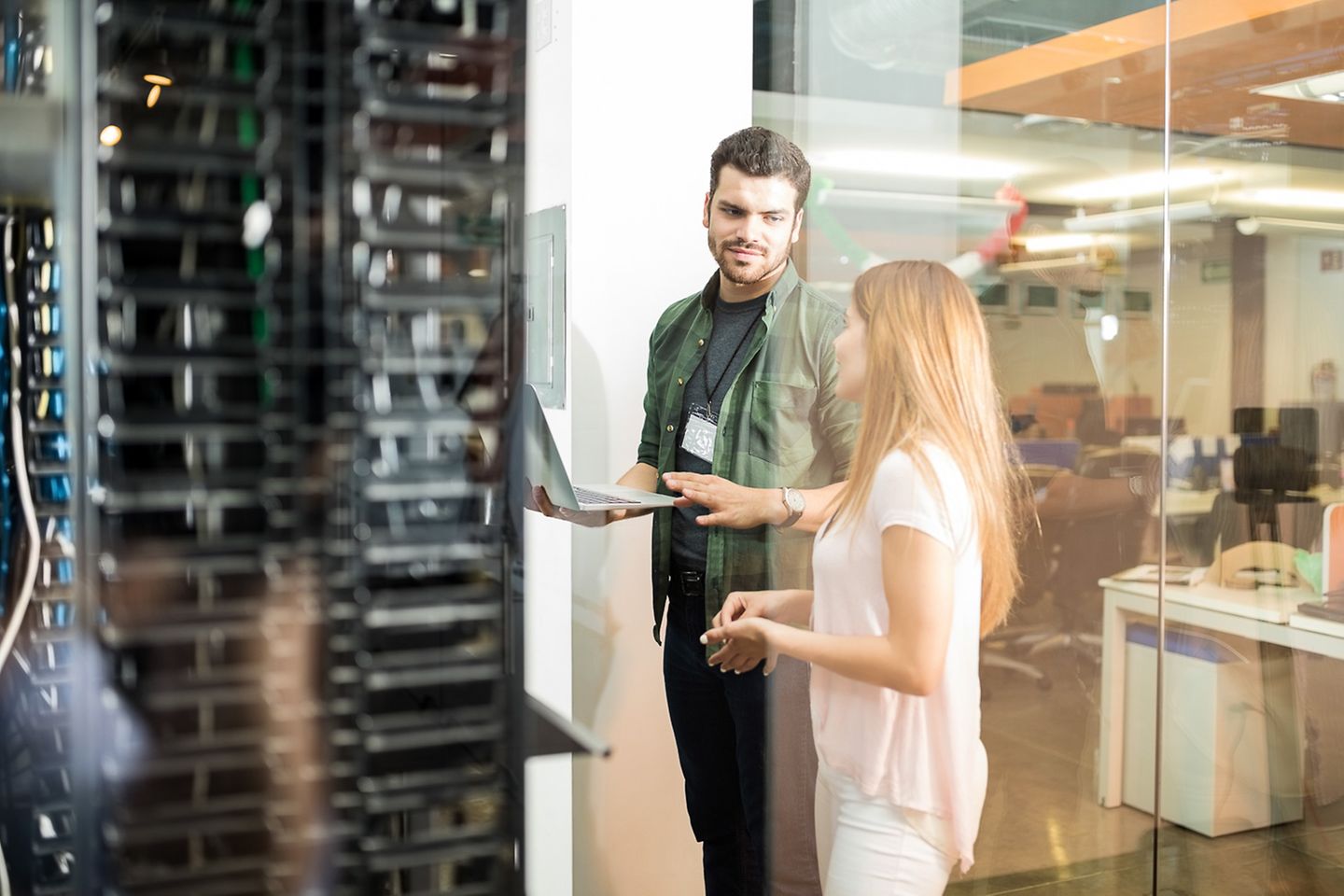 Zwei Kollegen stehen mit Laptop vor einem Server-Schrank und tauschen sich aus