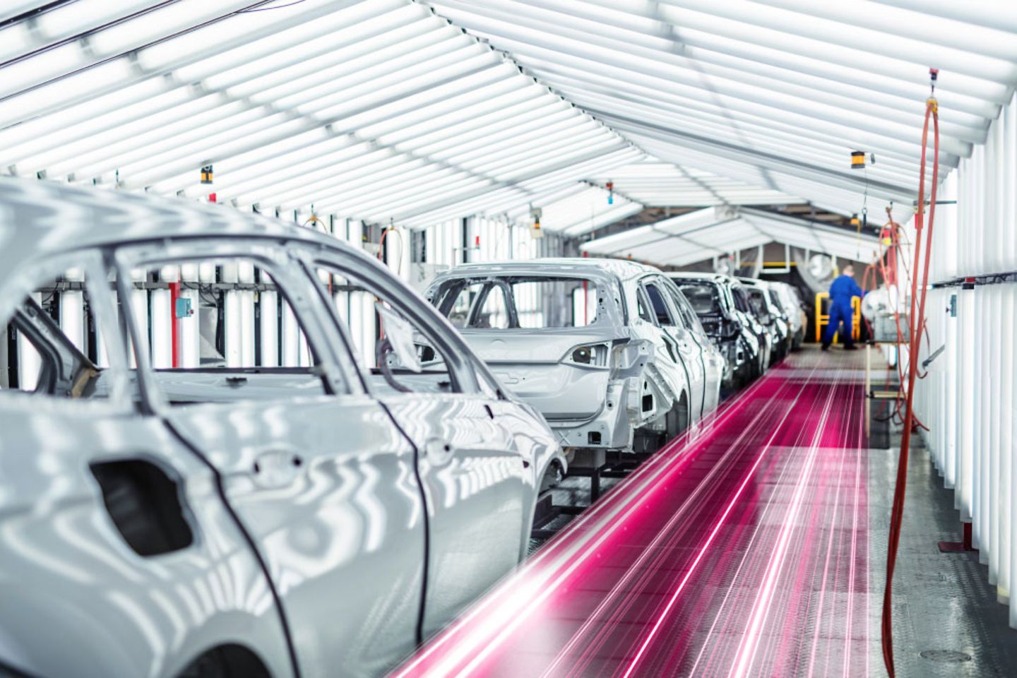 A row of car bodies in a factory next to magenta elements