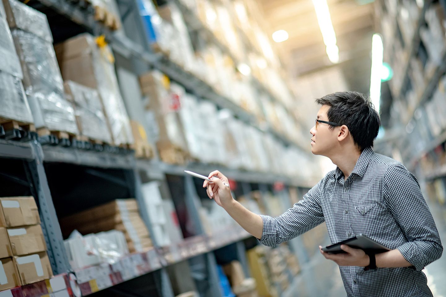 Young Asian man worker doing stocktaking in warehouse using digital tablet