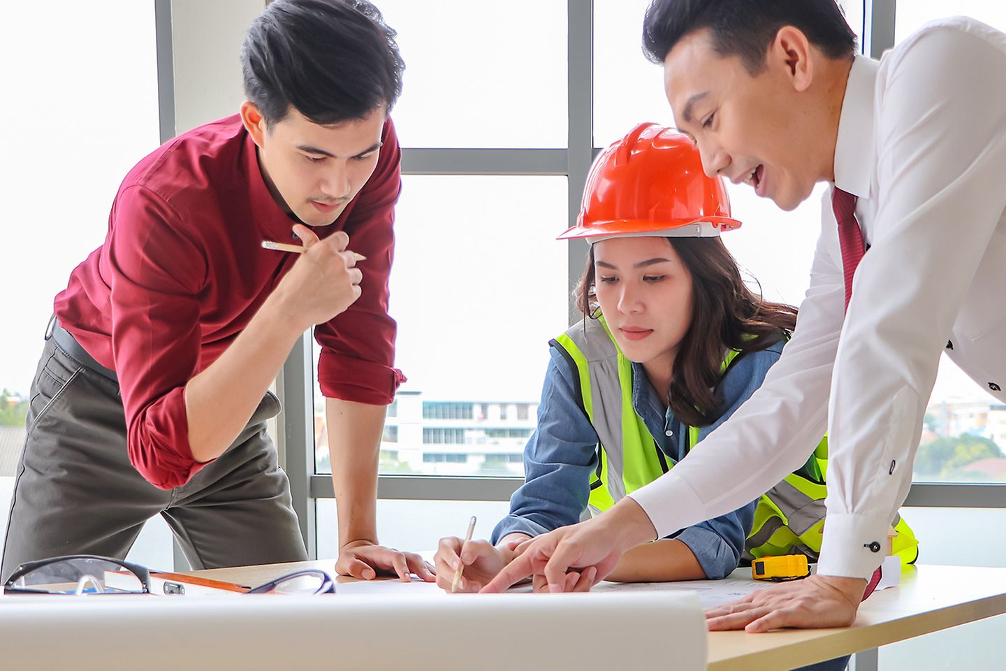 Two men in office wear and a woman in safety gear discussing a project at an office table