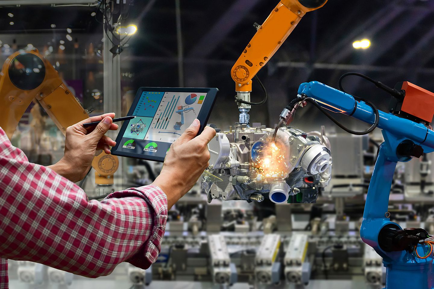 Engineer tapping a touch screen; in the background, mechanical arms manufacturing an engine