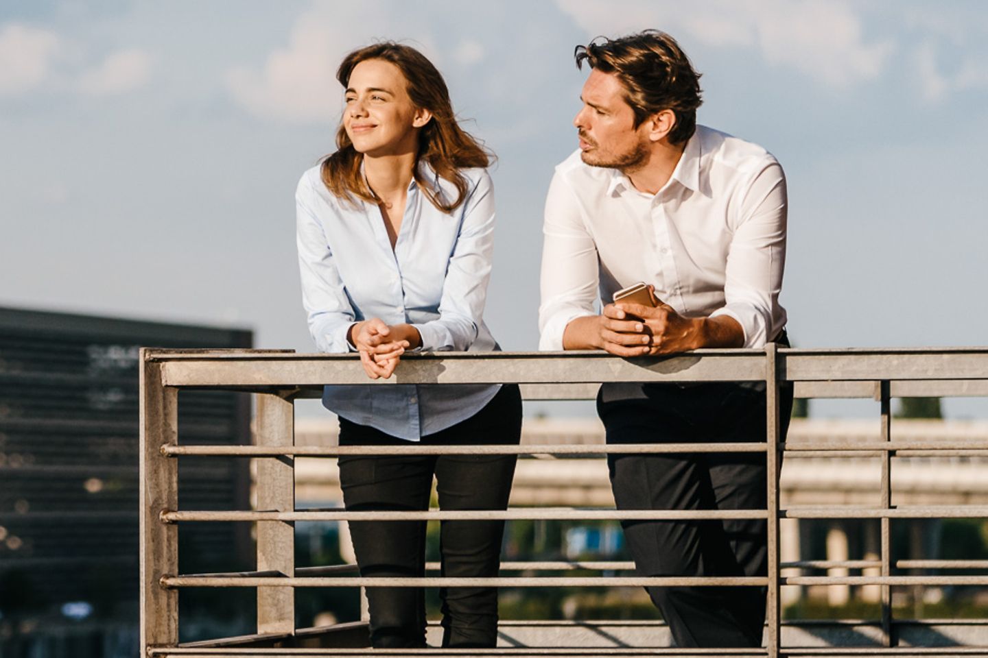 A man and a woman lean against a railing and look over a city