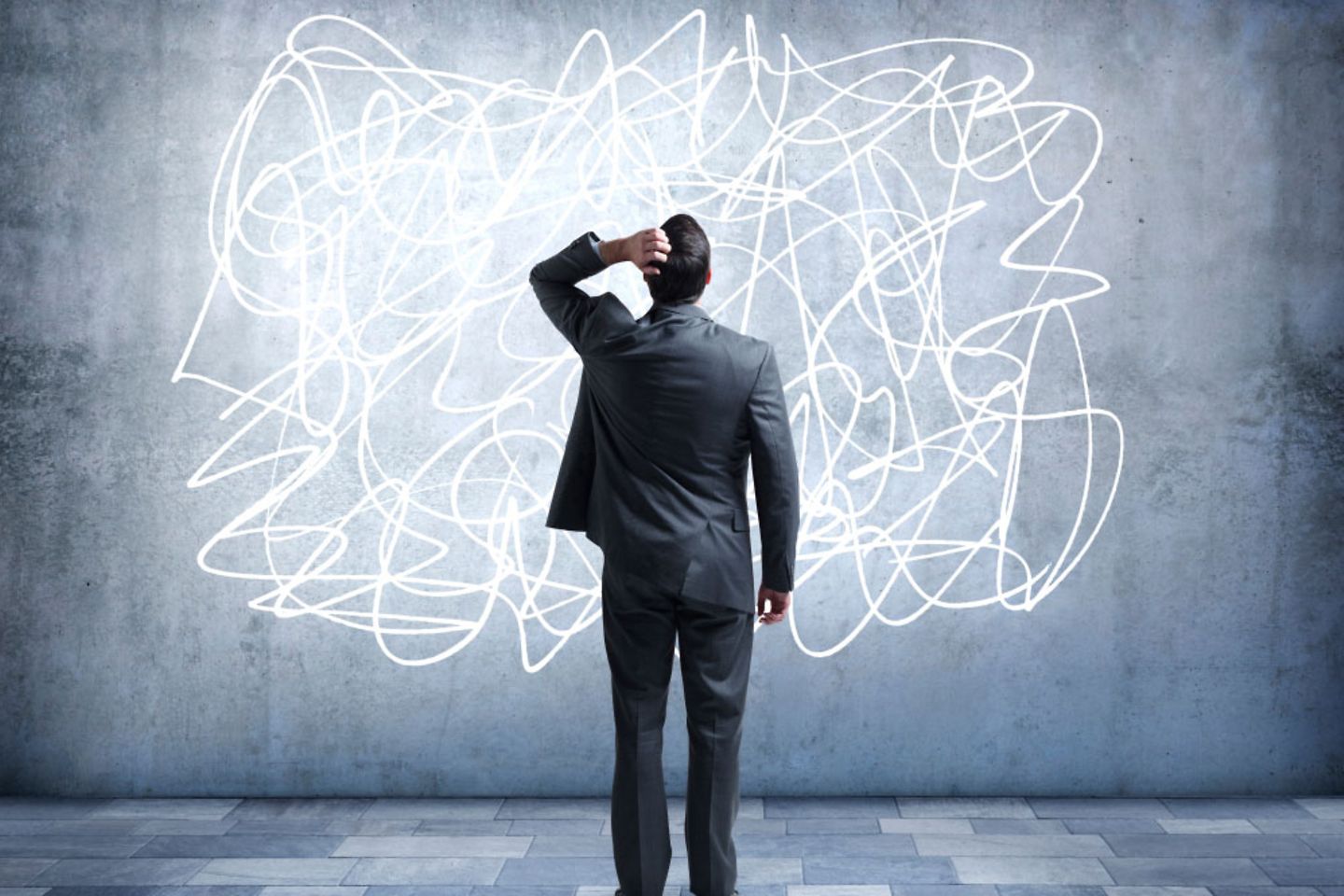 A man in a suit touches his head, stands in front of numerous lines 