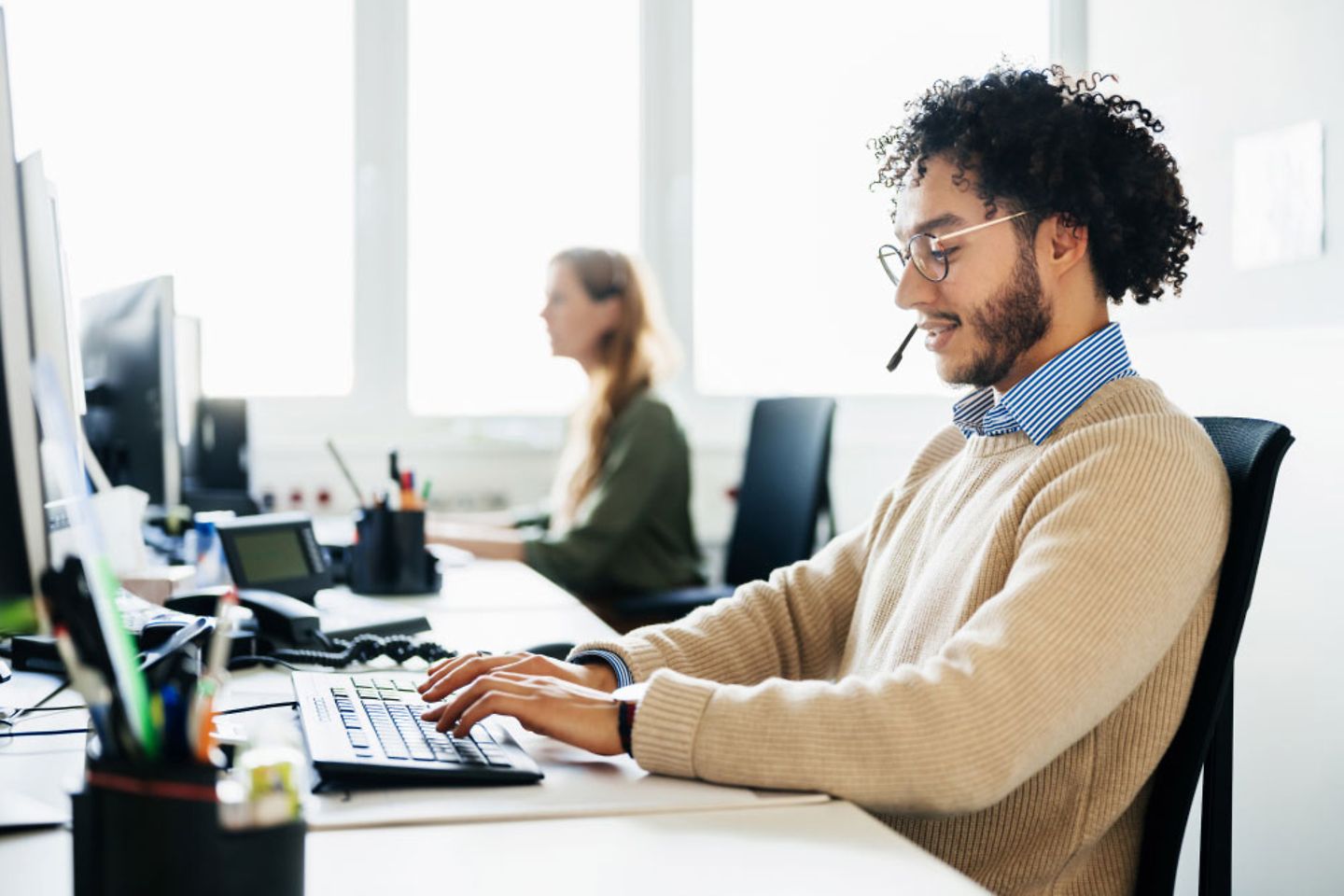 Um homem está trabalhando diante de um computador e falando com um cliente por um headset