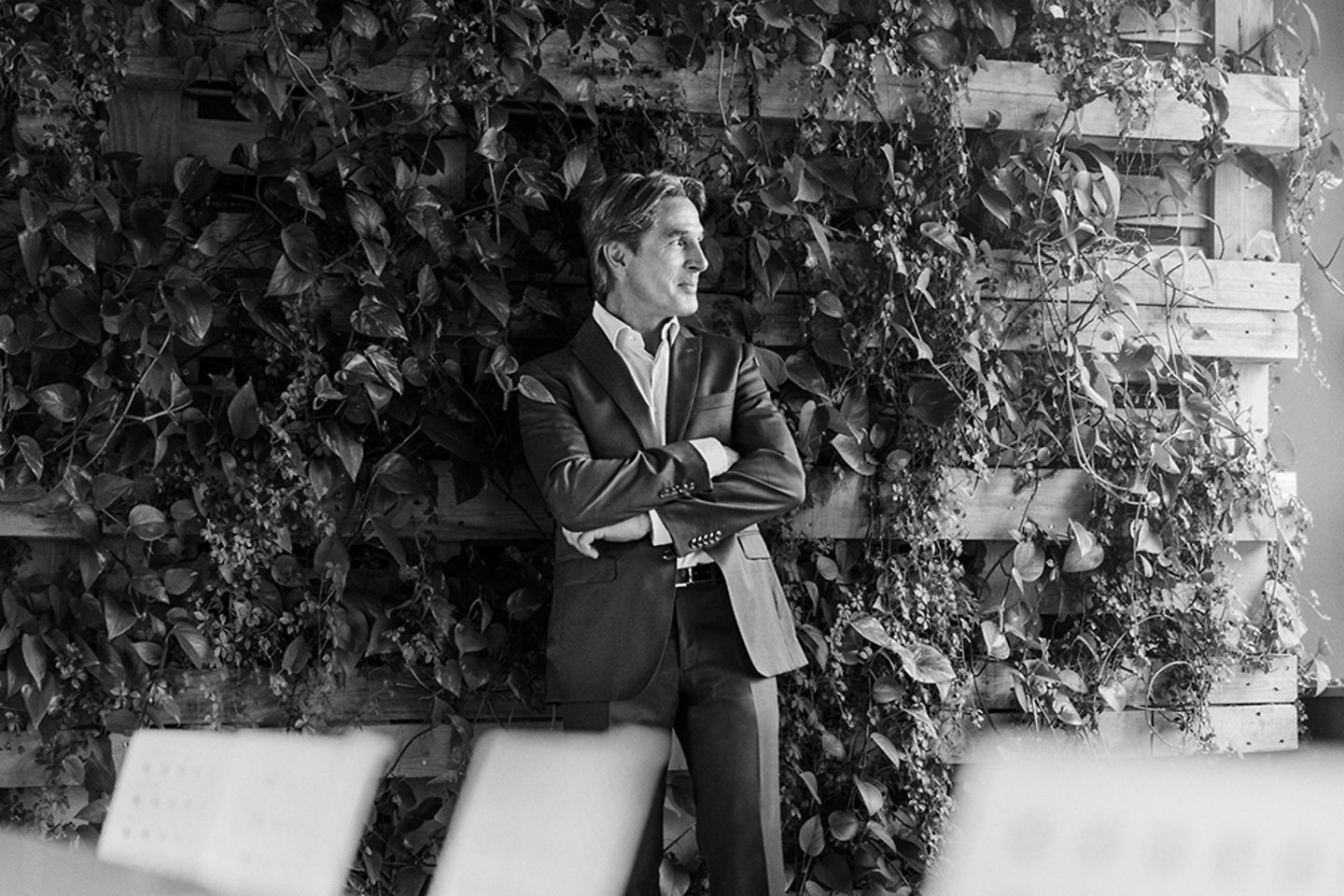 imagen en blanco y negro de un hombre de traje frente a una pared cubierta de vegetación