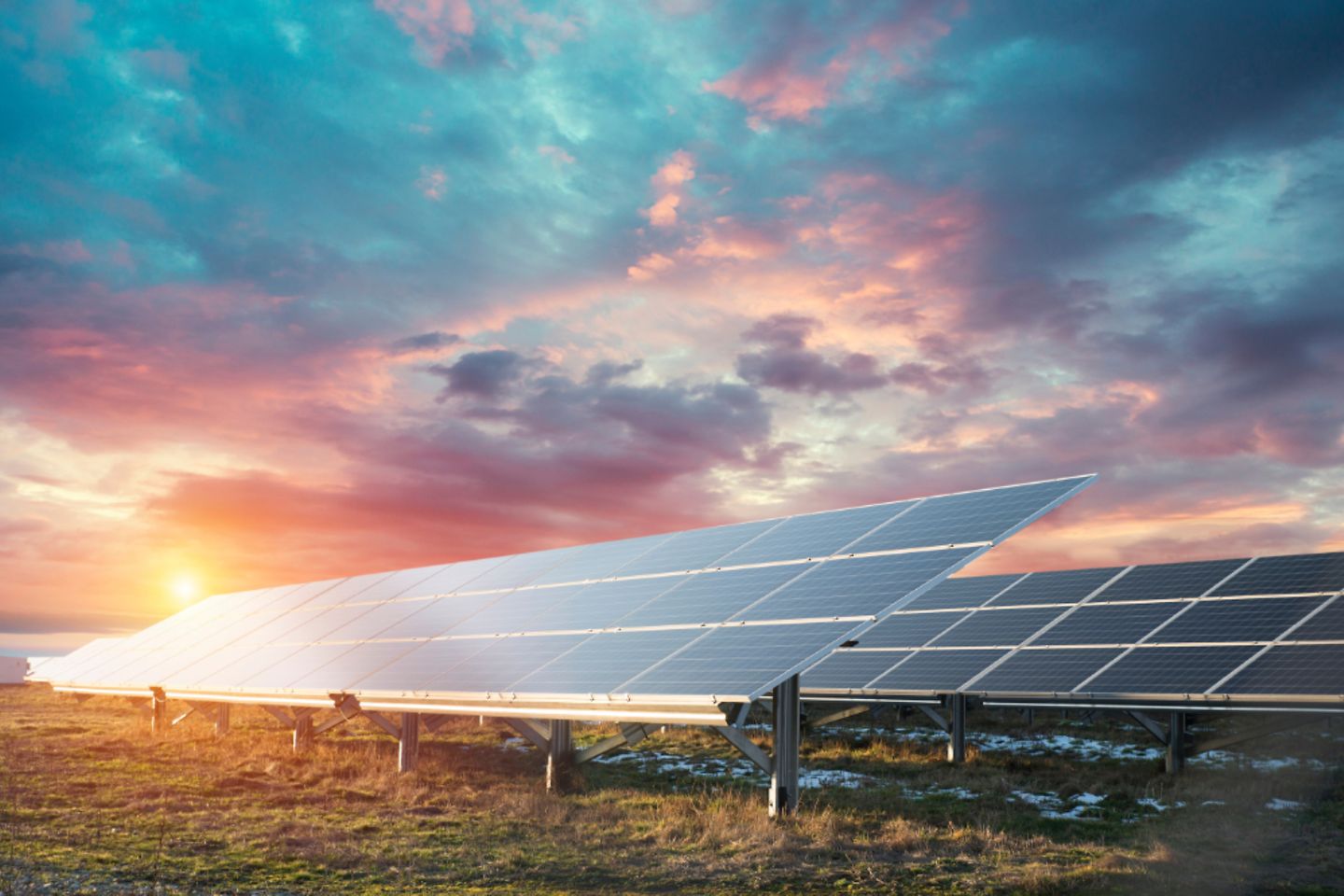 Photo of solar panels in grassy field with sunset background