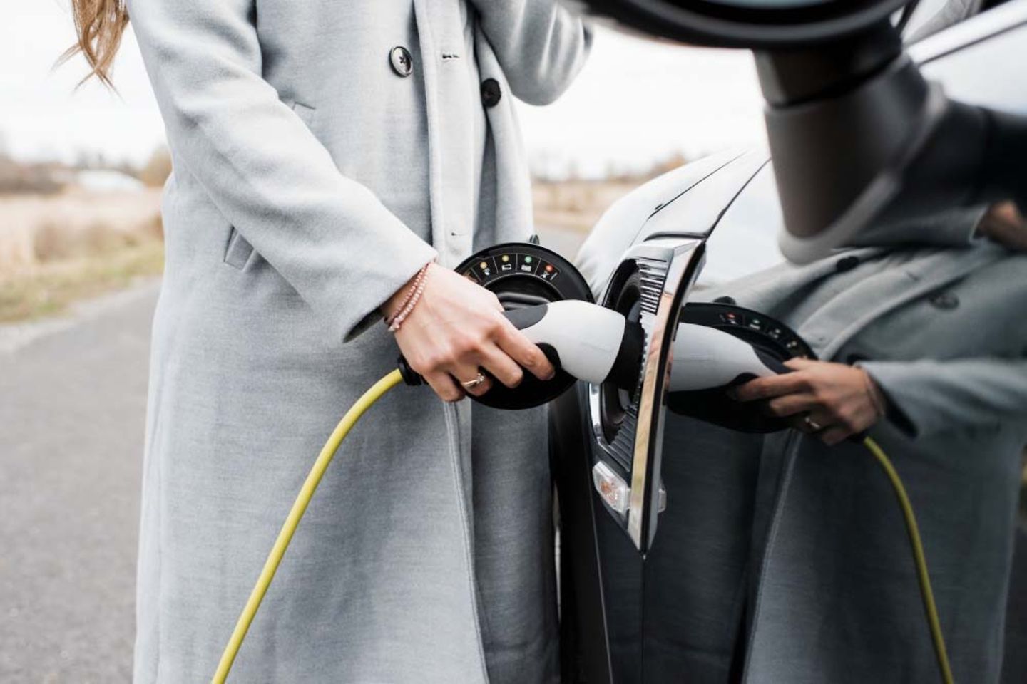 View of woman's hand plugging in charging lead to her electric car.