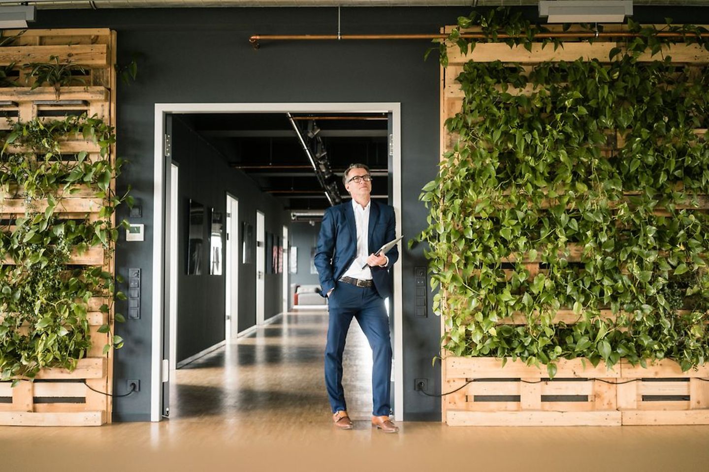 Man in pak staat in een grote deuropening, naast hem staan planten