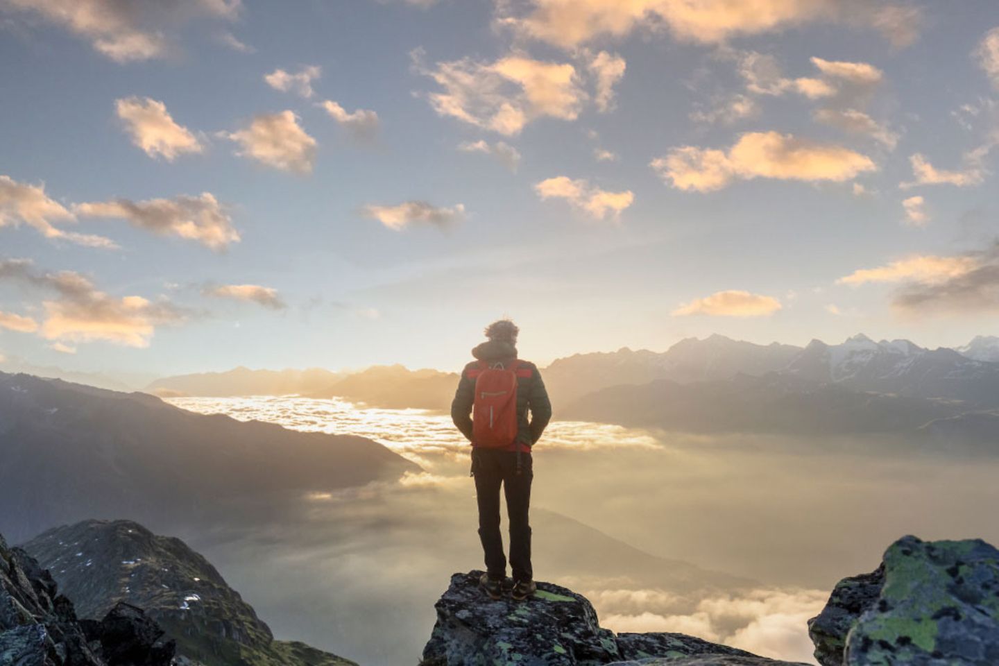 Ein Mann mit Wanderrucksack steht auf einem Berg und genießt die Aussicht