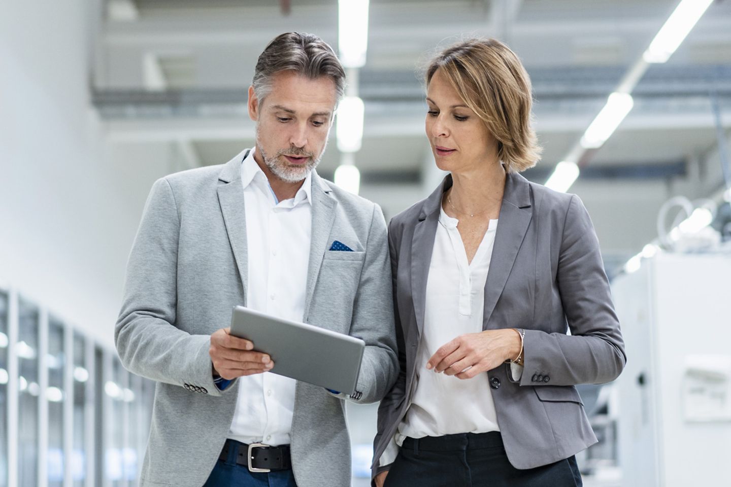 Businesswoman and businessman with tablet walking and talking in a modern factory