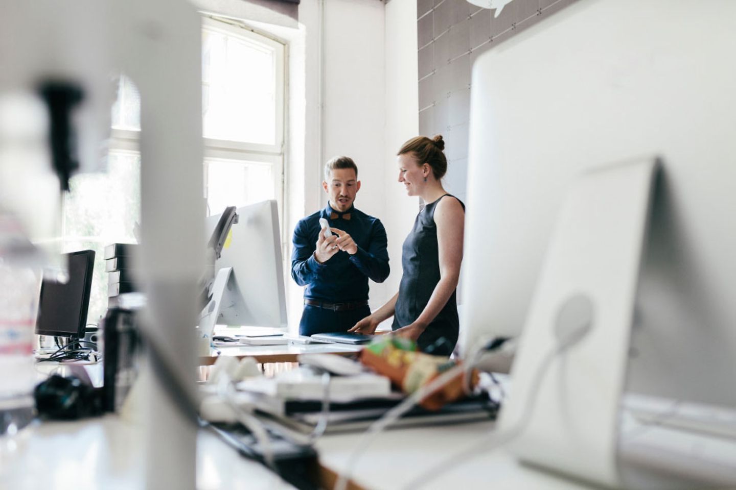 two colleagues are talking to each other in the office about a technical device