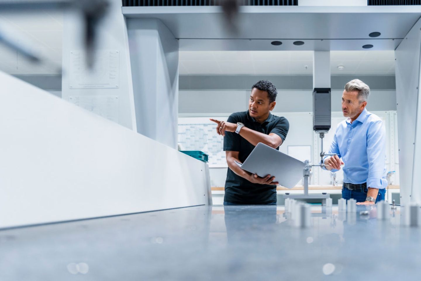 Engineer with laptop shows man in suit something in a manufacturing plant