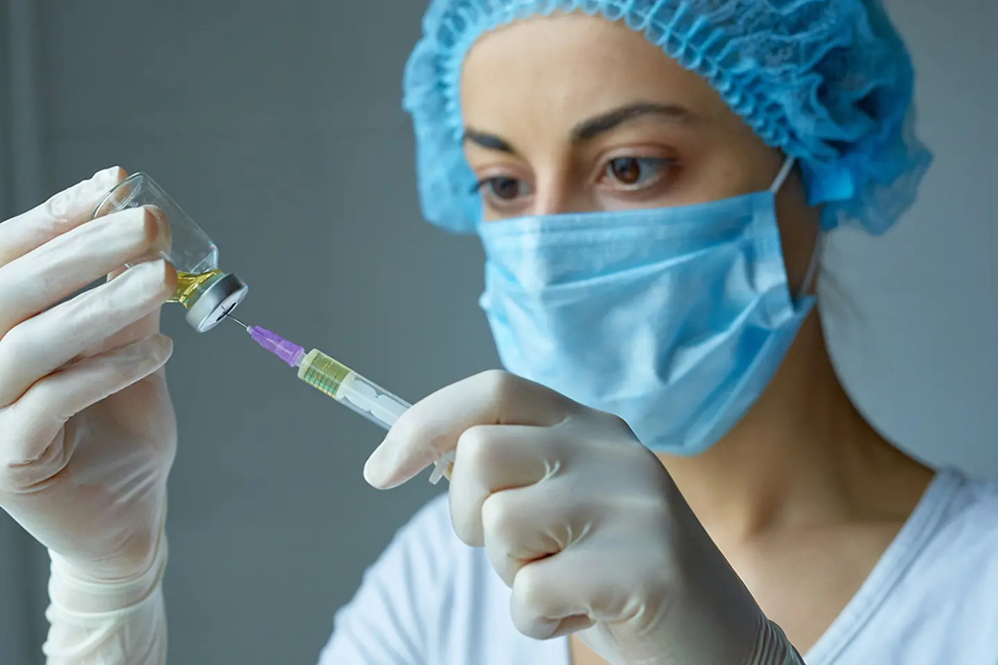 Krankenschwester mit Maske und Handschuhen, bereitet sich auf die Injektion vor, mit einer Spritze mit flüssigem Impfstoff.