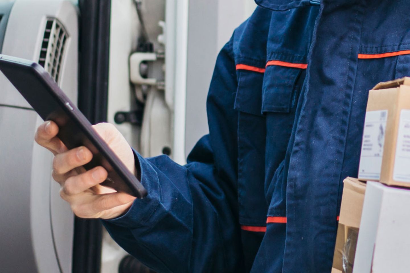 Een pakketbezorger met pakjes in de ene hand en een tablet in de andere