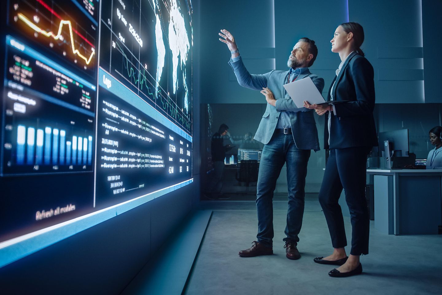 Man explaining something to woman while pointing at huge screen