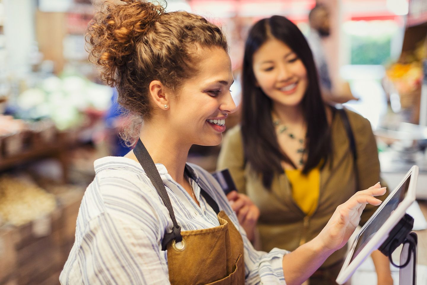 Verkäuferin hilft Kundin an einem Touchscreen einer digitalen Kasse in einem Supermarkt