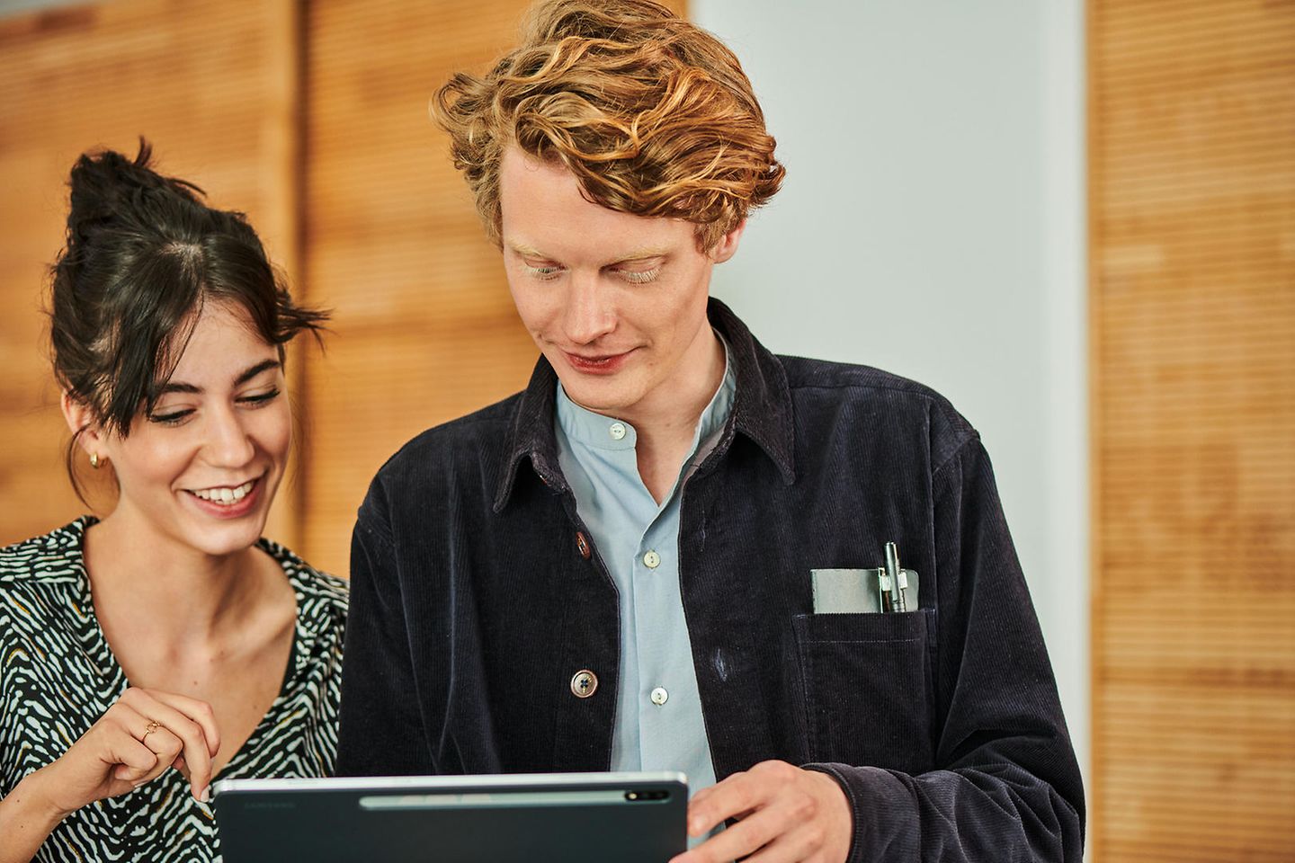 A man and a woman are looking at an iPad together, smiling.