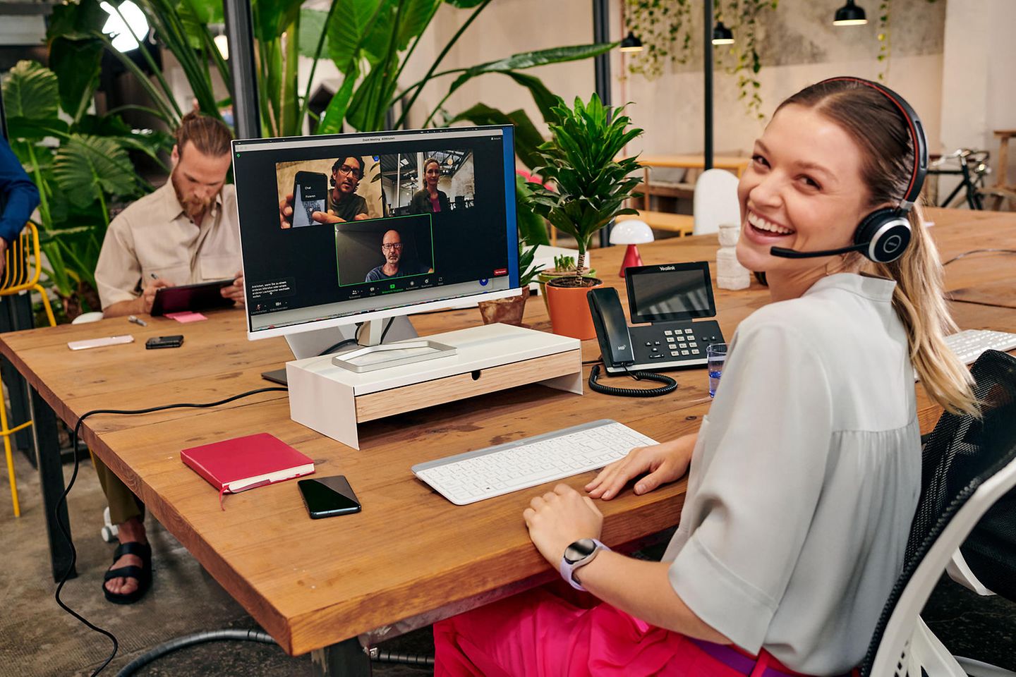 A woman sits in an office and takes part in a video conference. She smiles at the camera.