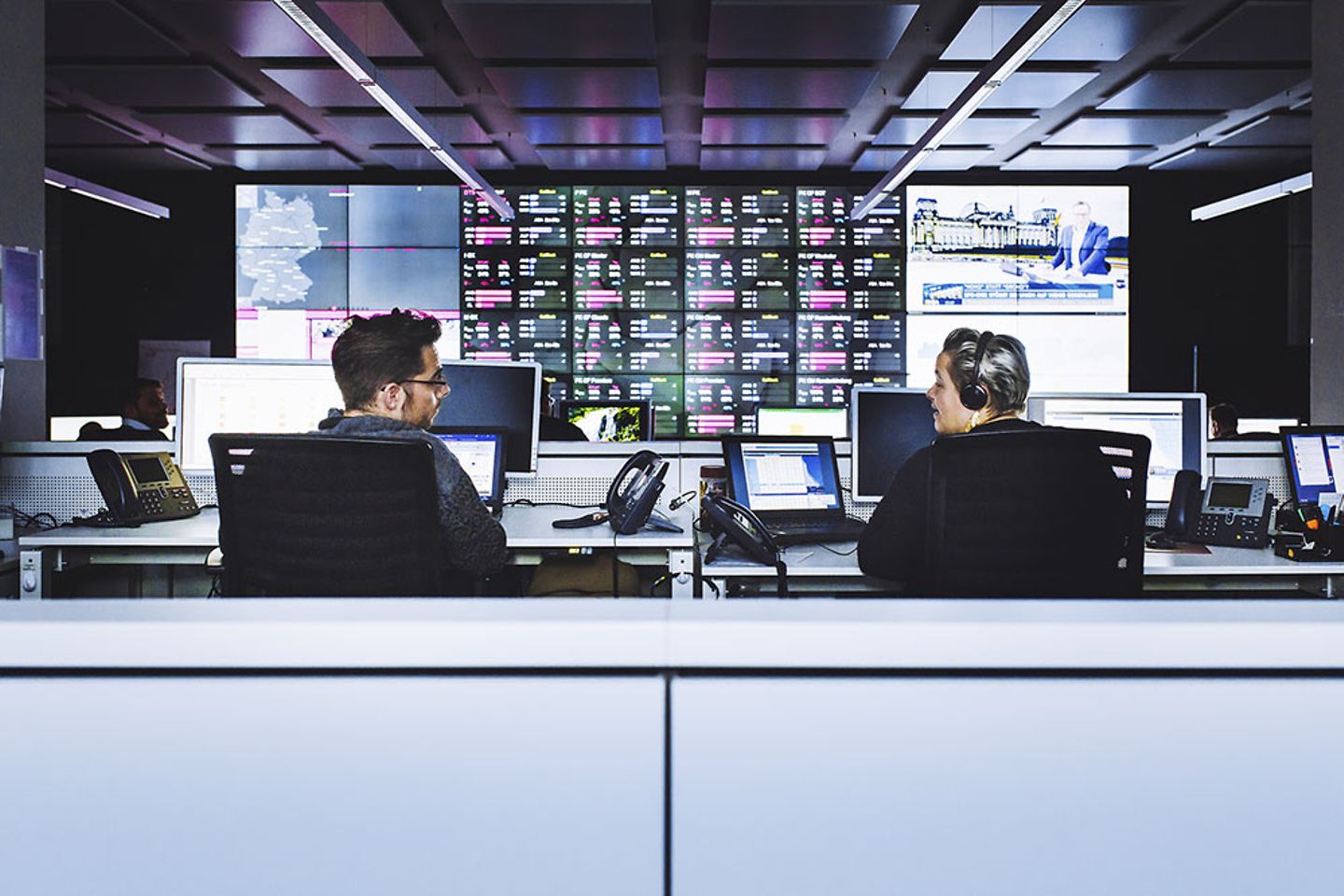 A man and a woman sit in front of a wall full of screens