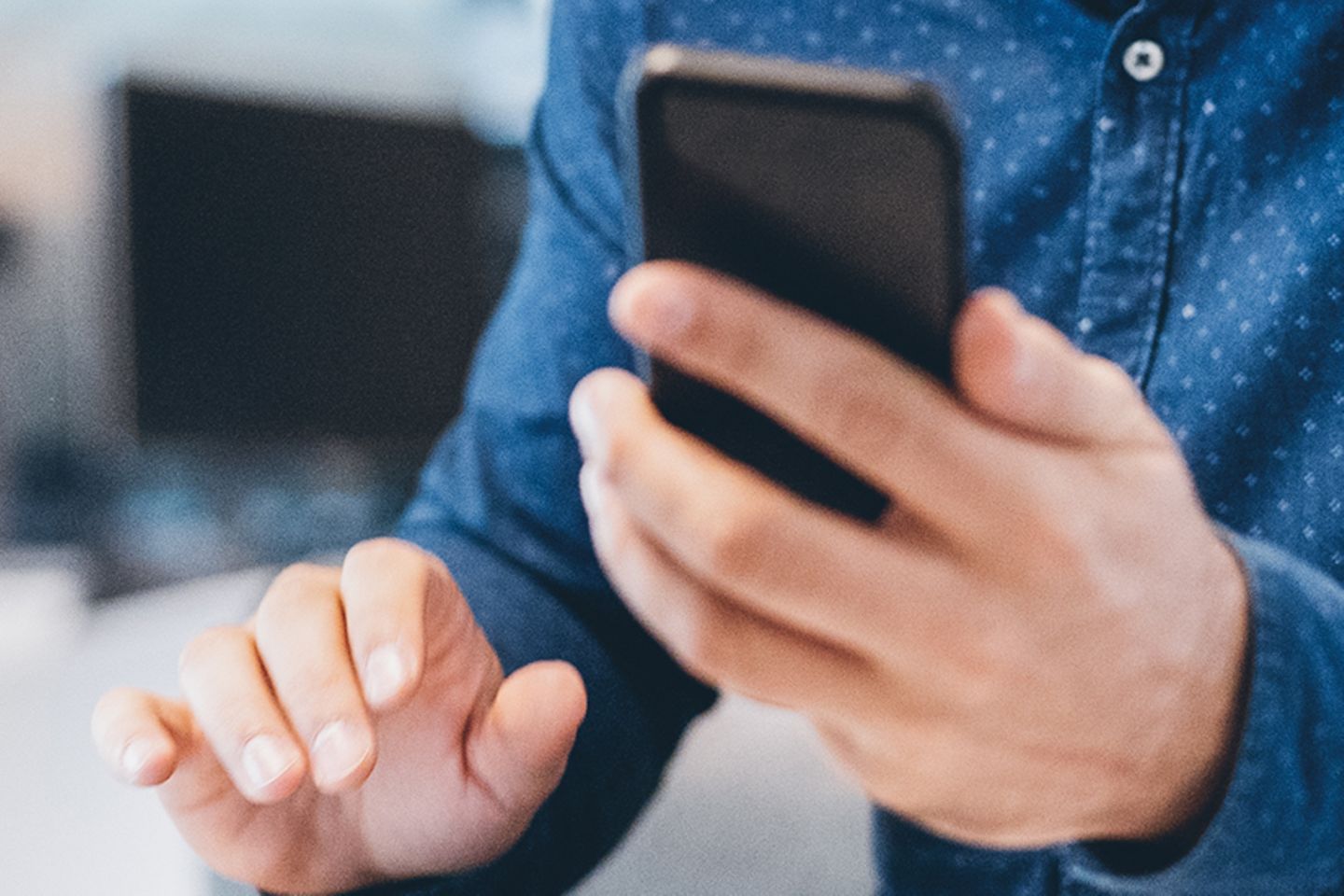 A man in a shirt in front of a tabltop and smartphone in hand