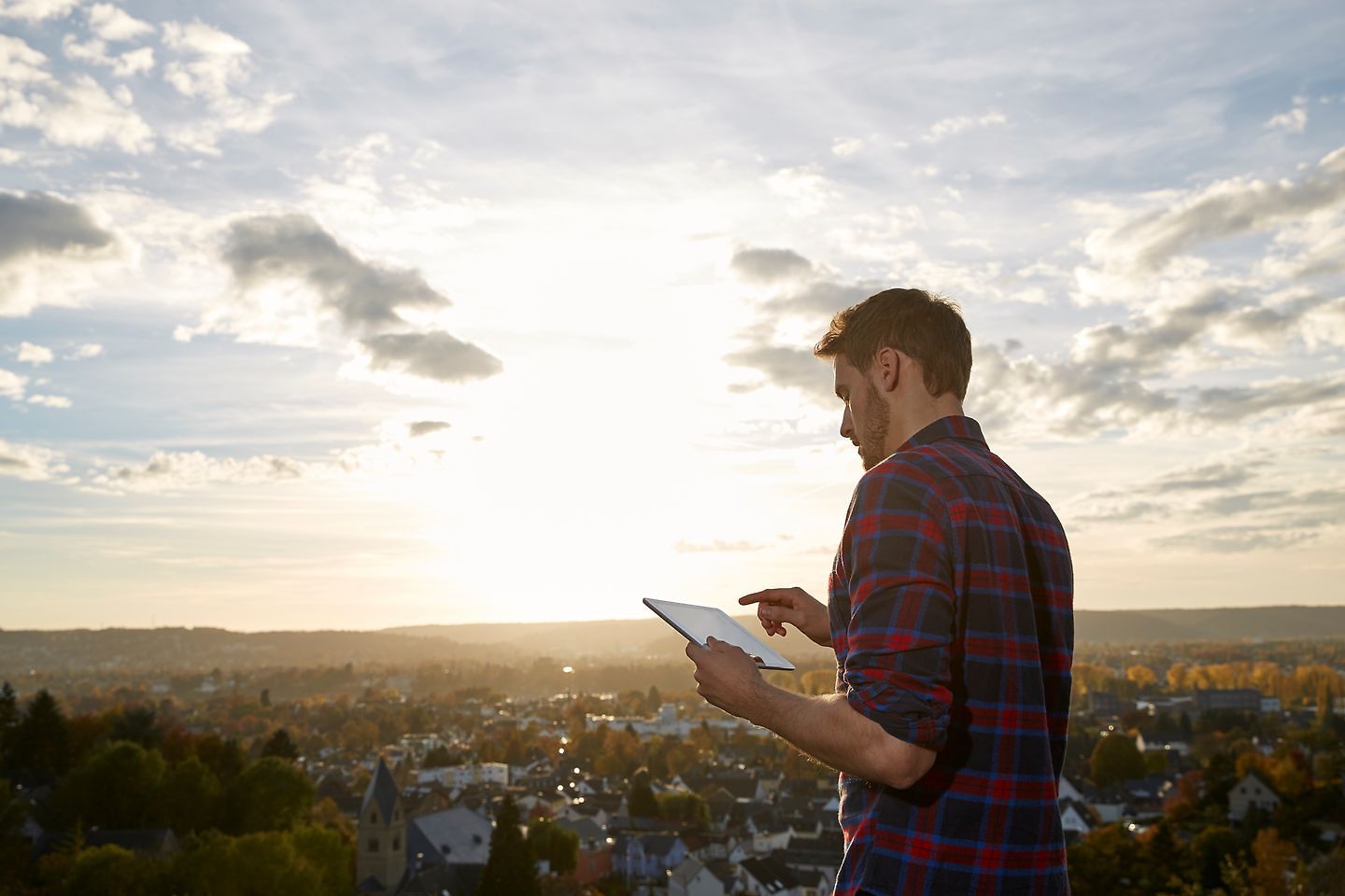 A man looks at a tablet with a view of a city in the background