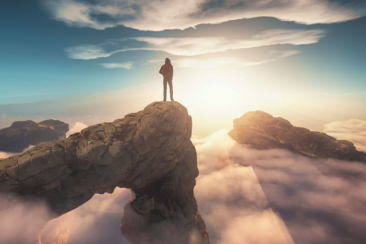 Um homem está no pico de uma montanha acima da cobertura de nuvens