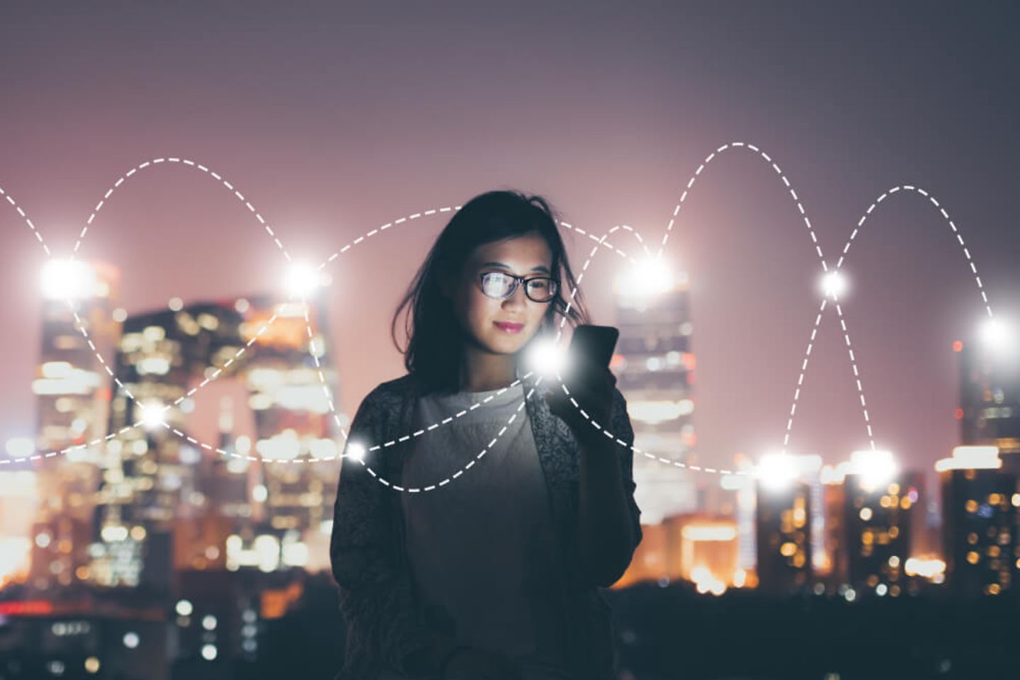 Woman with smartphone in front of skyline at night