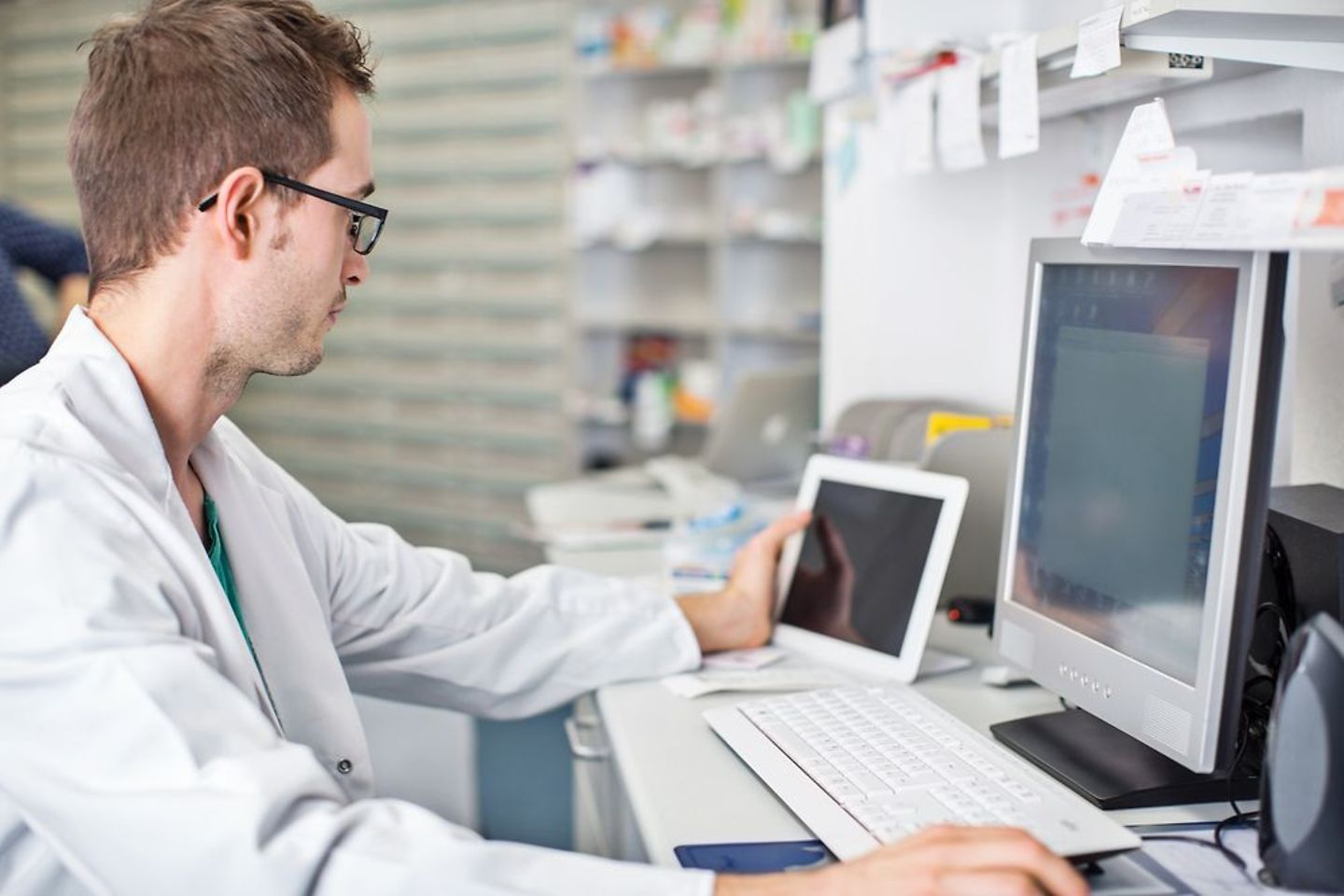 Man in lab coat works on computer and tablet