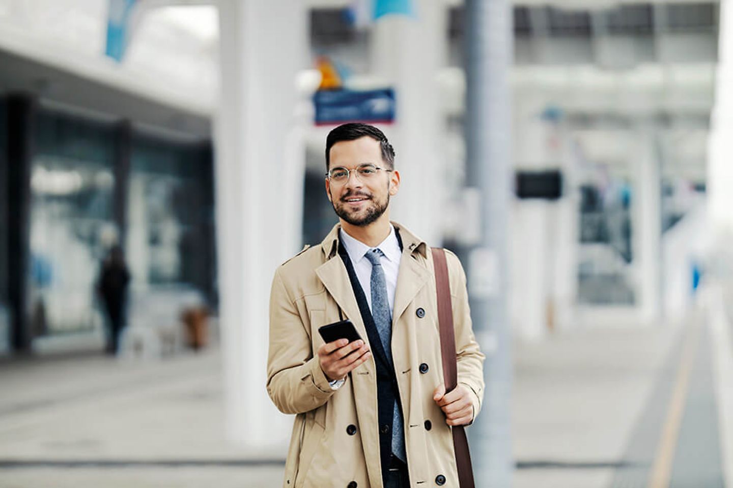 Mann im Business Outfit steht mit Smartphone in der Hand am Gleis