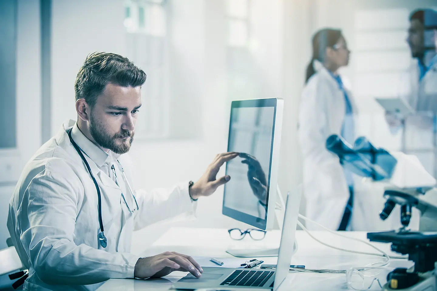 Patientendaten auf einem aufgeklappten Laptop und ein Arzt der diese anschaut 