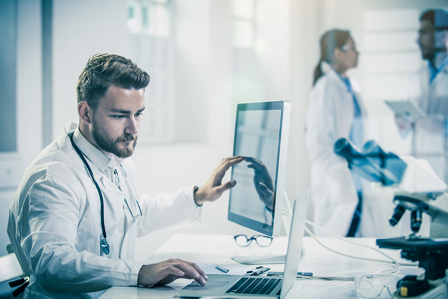 Patientendaten auf einem aufgeklappten Laptop und ein Arzt der diese anschaut 