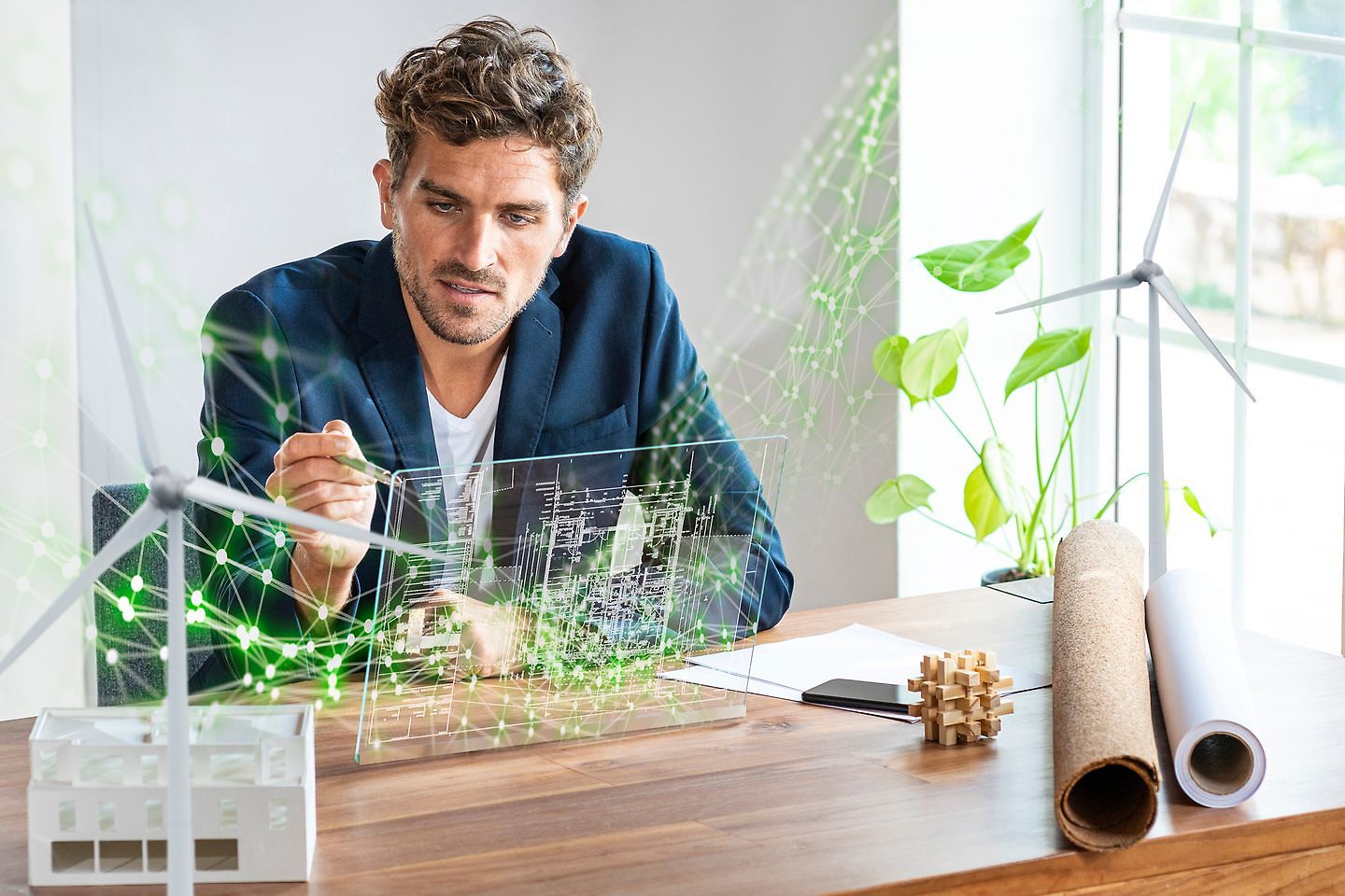 Hombre en una oficina mirando a una pantalla futurista con un plano de una casa sostenible y aerogeneradores