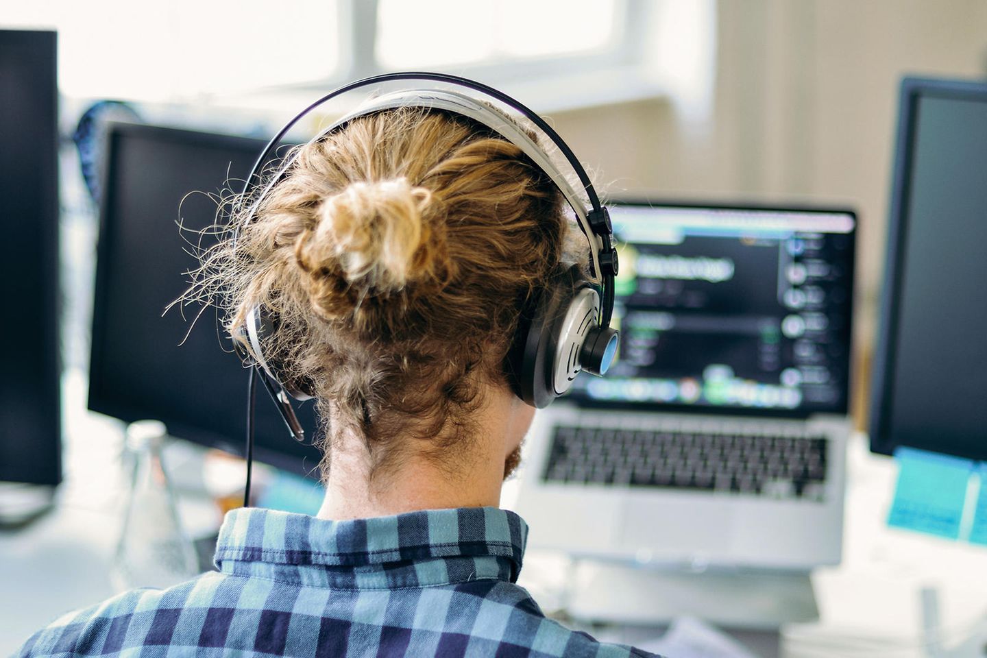 Blick von hinten auf einen jungen Mann mit Over-Ear Kopfhörer vor einem Notebook