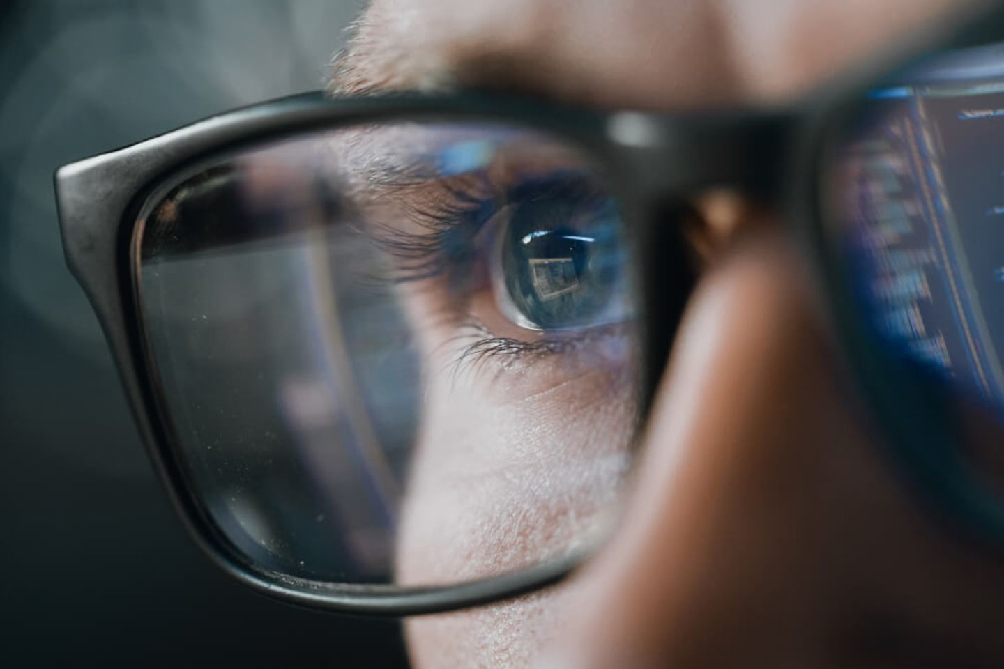 Retrato en primer plano de un ingeniero de software trabajando en una computadora, código que se refleja en unos lentes.