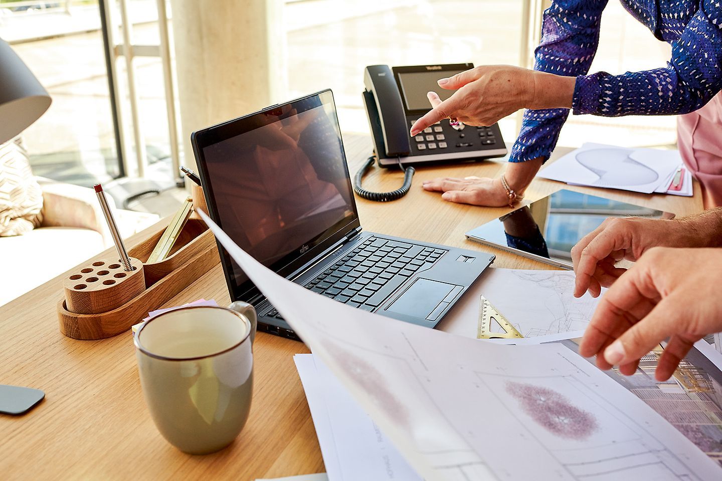 Close up desk with laptop, paperwork and gesticulating hands