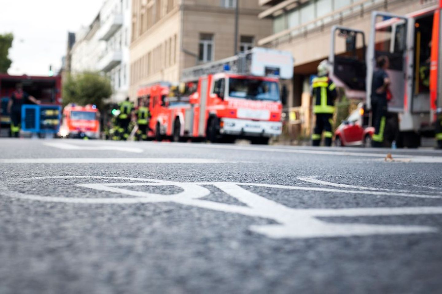 Unrecognisable firefighters and fire trucks at place of action, low-angle view, selective focus