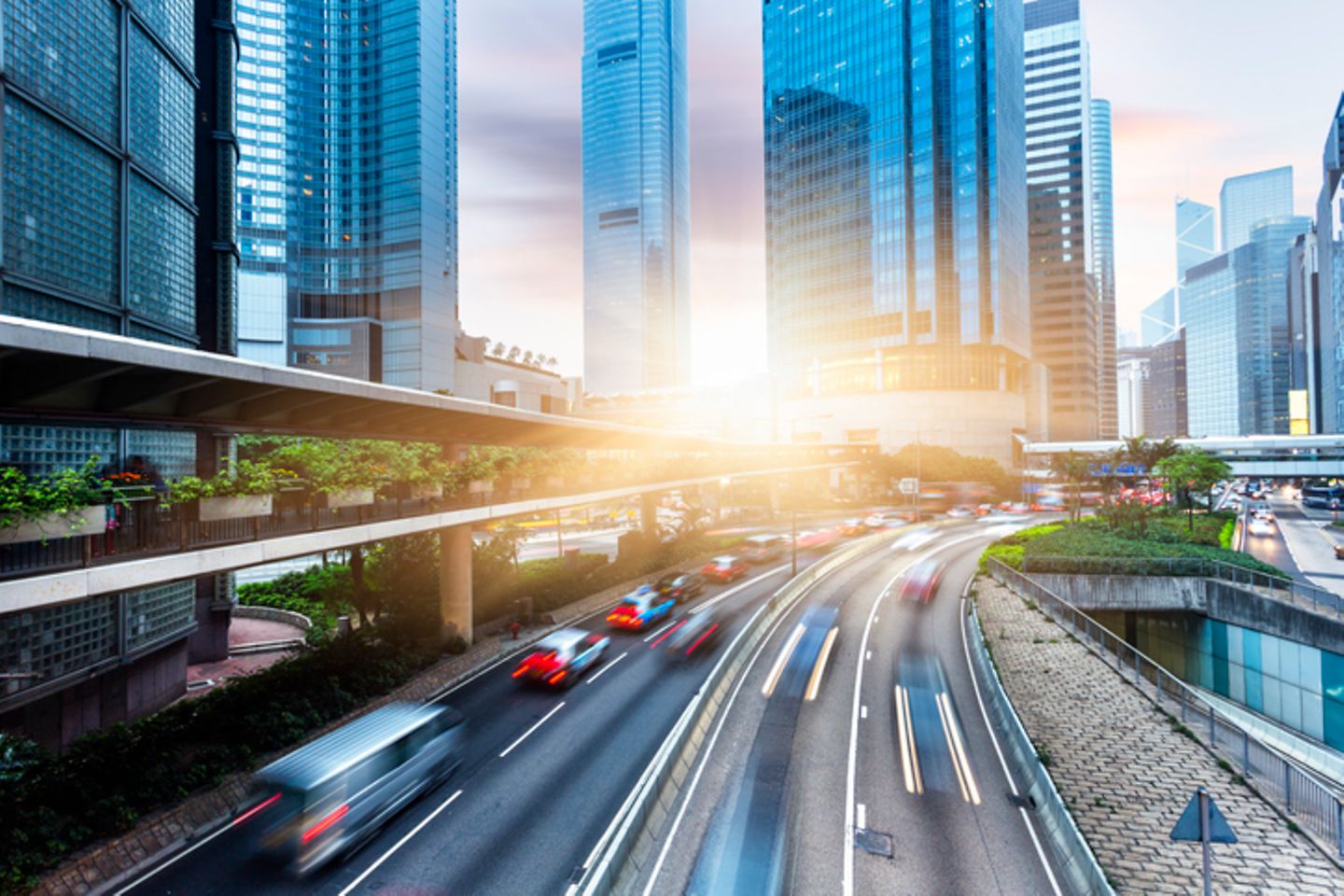 Multi-lane road in front of skyscrapers with blinding sun in the middle of the picture