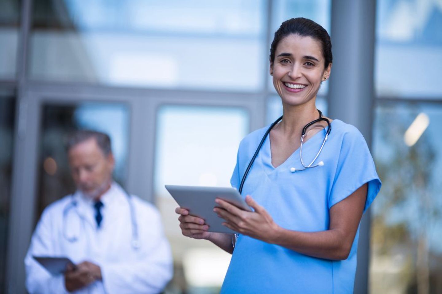 Doctora-enfermera sonriente con tableta electrónica en el exterior de un hospital