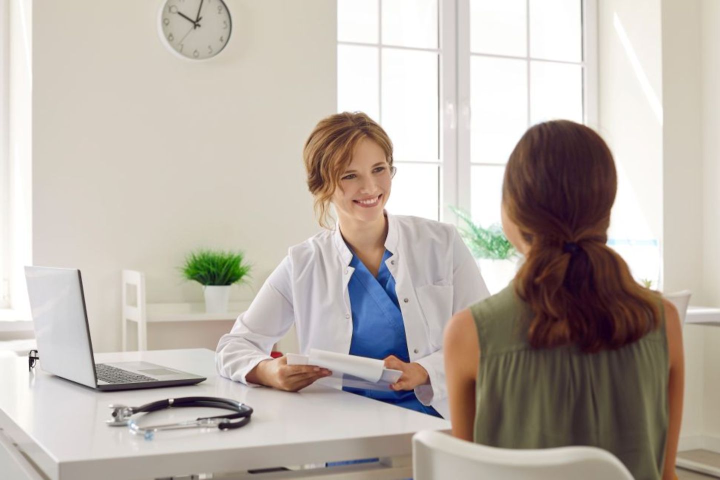 Doctora charlando con una paciente mientras consulta su expediente en el ordenador