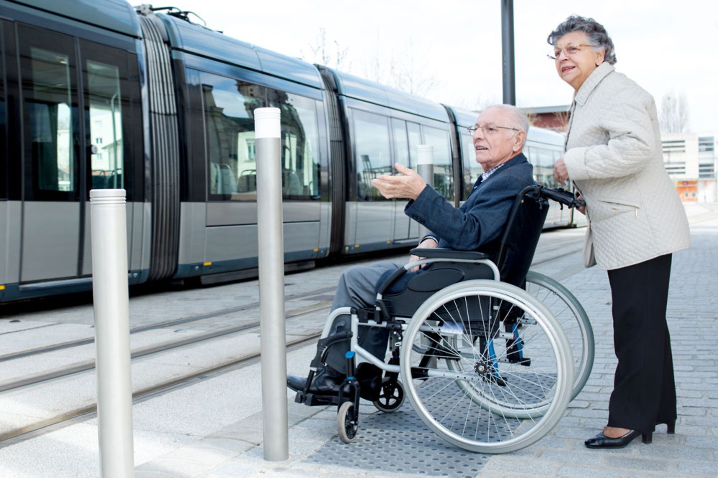 Pareja de ancianos esperando el tren en silla de ruedas, infraestructura de transporte público